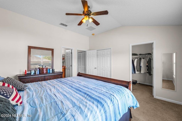 carpeted bedroom featuring a textured ceiling, two closets, ceiling fan, and lofted ceiling