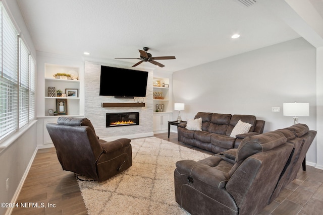 living room featuring built in shelves, a large fireplace, hardwood / wood-style flooring, and ceiling fan