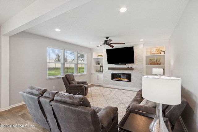 living room featuring built in shelves, ceiling fan, a large fireplace, and light hardwood / wood-style flooring