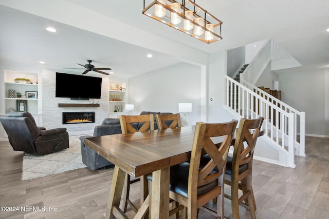 dining room featuring a fireplace, light hardwood / wood-style flooring, built in features, and ceiling fan