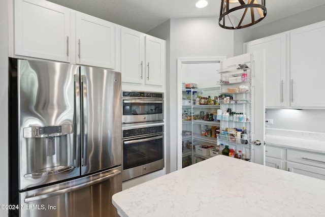 kitchen with white cabinets, appliances with stainless steel finishes, light stone countertops, and hanging light fixtures