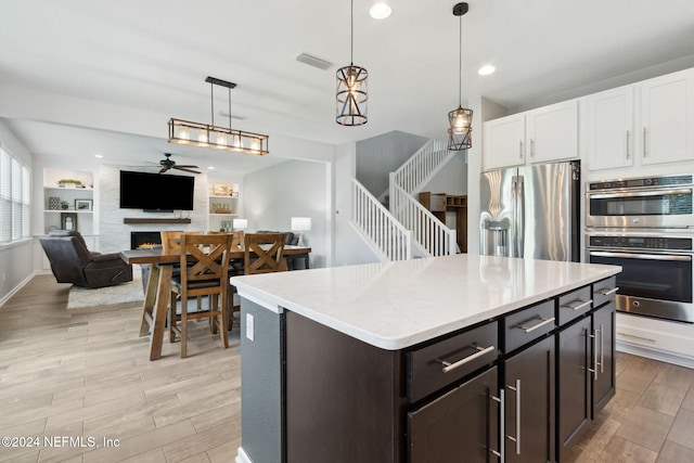 kitchen with ceiling fan, pendant lighting, a fireplace, white cabinets, and appliances with stainless steel finishes