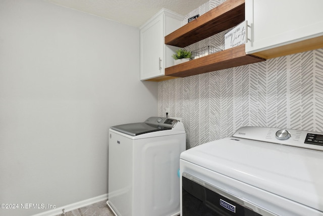 laundry room with cabinets, a textured ceiling, and washing machine and clothes dryer