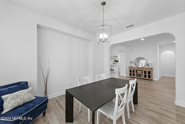 dining space with built in shelves, light hardwood / wood-style flooring, and a notable chandelier