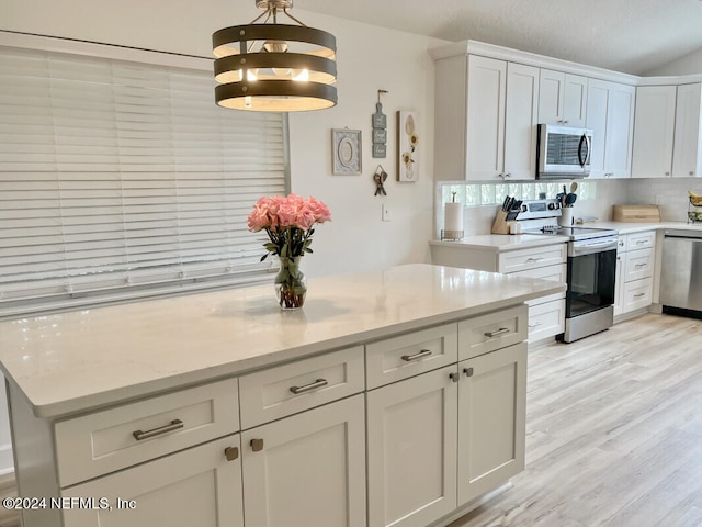 kitchen with hanging light fixtures, light stone countertops, light wood-type flooring, white cabinetry, and stainless steel appliances