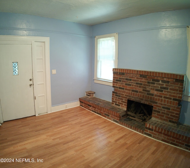 unfurnished living room featuring a brick fireplace and light wood-type flooring