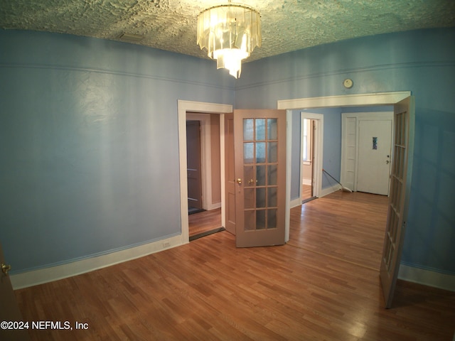 unfurnished room with a chandelier, wood-type flooring, a textured ceiling, and french doors