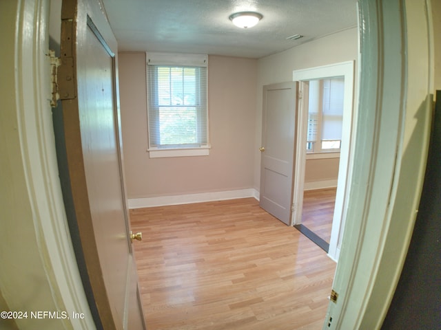 corridor with light hardwood / wood-style floors and a textured ceiling