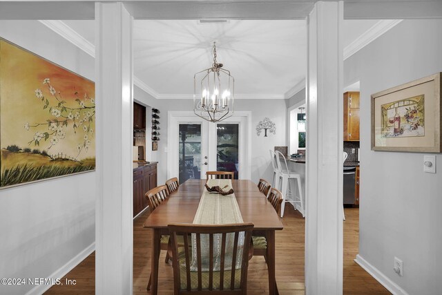 dining space with hardwood / wood-style flooring, an inviting chandelier, crown molding, and french doors