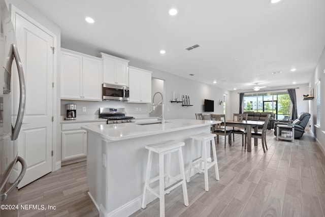 kitchen featuring a center island with sink, white cabinets, stainless steel appliances, and light hardwood / wood-style flooring