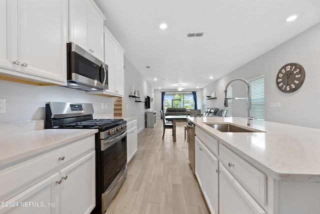 kitchen with stainless steel appliances, sink, light hardwood / wood-style flooring, white cabinets, and an island with sink