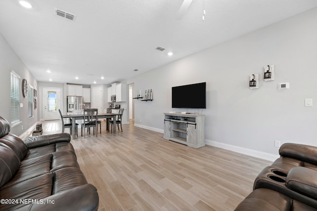 living room with ceiling fan, a textured ceiling, and light hardwood / wood-style flooring