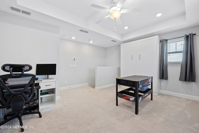 carpeted office space with a tray ceiling and ceiling fan