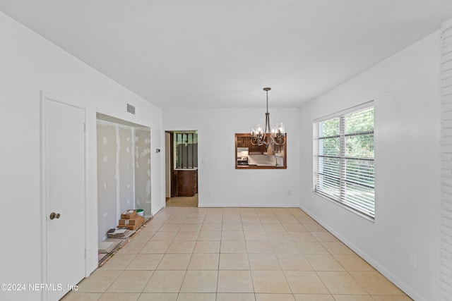 tiled spare room featuring a chandelier