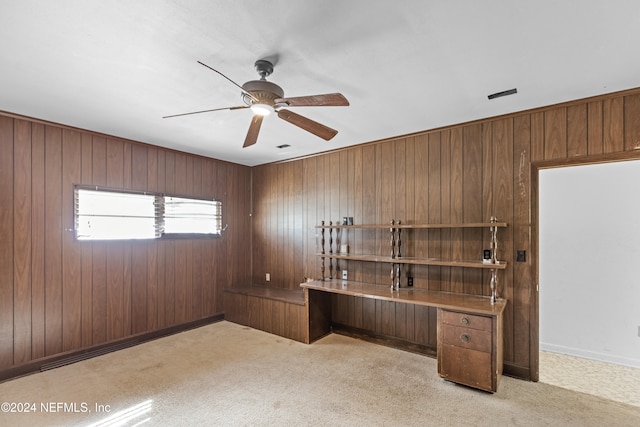 unfurnished office featuring light carpet, ceiling fan, and wood walls