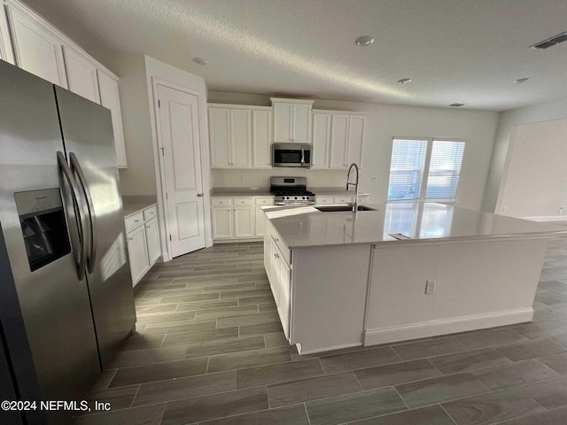 kitchen featuring stainless steel appliances, white cabinetry, a center island with sink, and sink