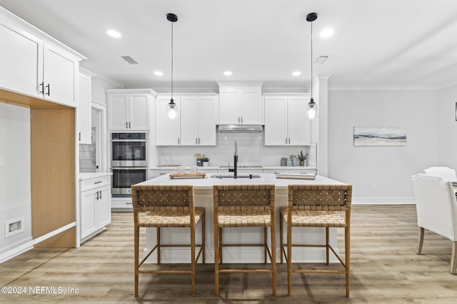 kitchen with decorative light fixtures, stainless steel double oven, and an island with sink