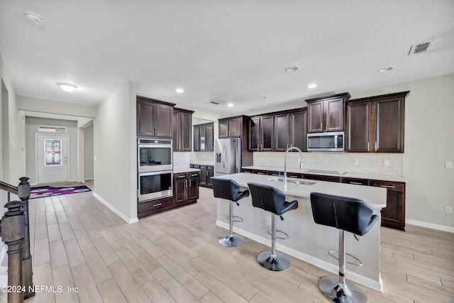 kitchen with light hardwood / wood-style flooring, sink, stainless steel appliances, and an island with sink