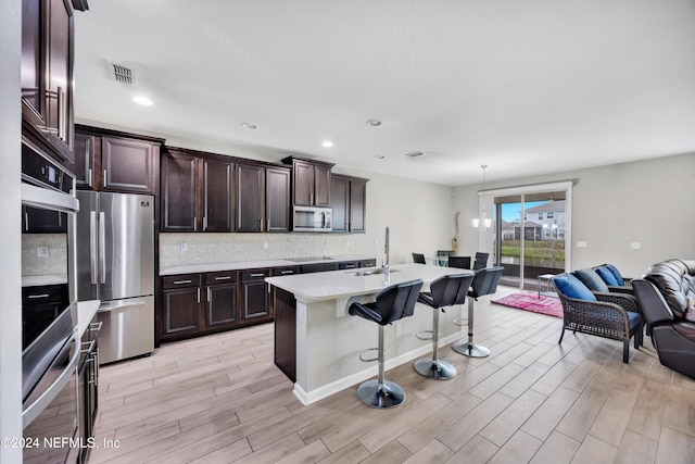 kitchen with sink, stainless steel appliances, a kitchen bar, a center island with sink, and light wood-type flooring