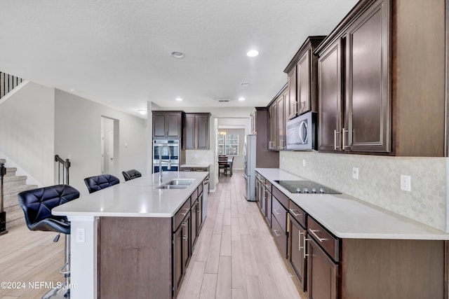 kitchen featuring sink, a breakfast bar area, dark brown cabinets, appliances with stainless steel finishes, and light wood-type flooring