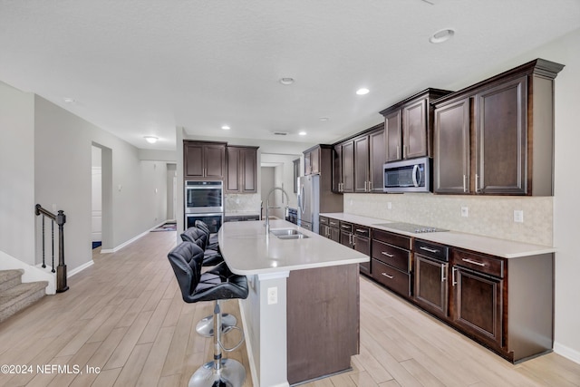 kitchen featuring dark brown cabinetry, sink, stainless steel appliances, a center island with sink, and light wood-type flooring