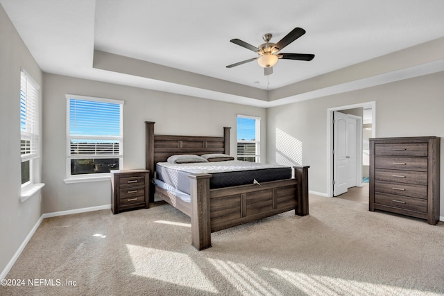 carpeted bedroom with a tray ceiling, ensuite bath, and ceiling fan