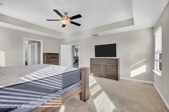 bedroom featuring a raised ceiling, ceiling fan, light colored carpet, and connected bathroom