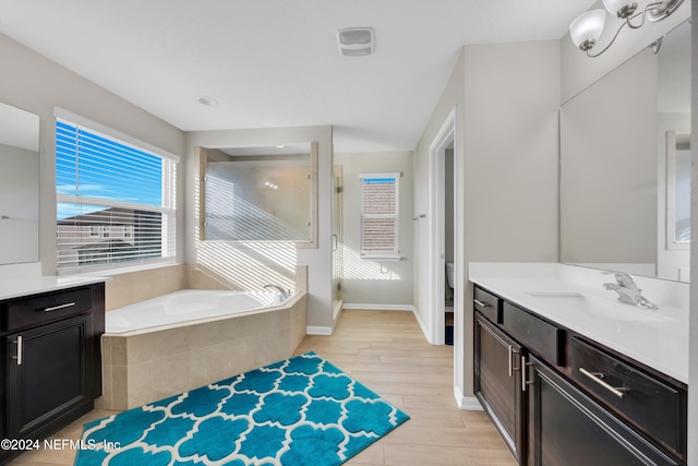 bathroom with tiled bath, toilet, vanity, and hardwood / wood-style flooring