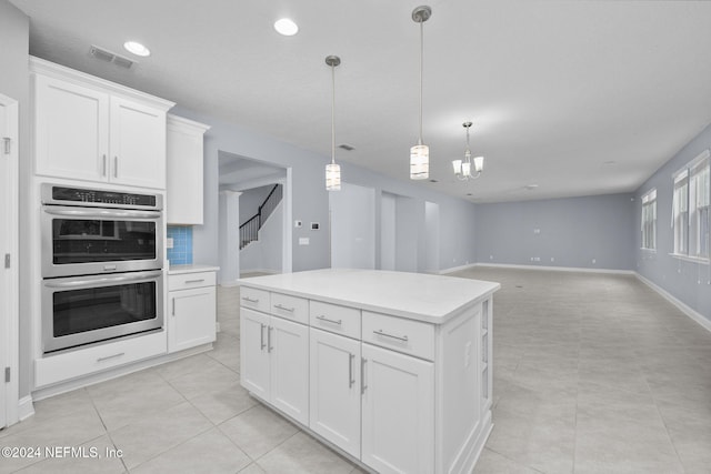 kitchen featuring a center island, hanging light fixtures, stainless steel double oven, light tile patterned floors, and white cabinets