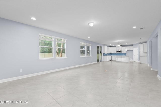 unfurnished living room with light tile patterned flooring and an inviting chandelier