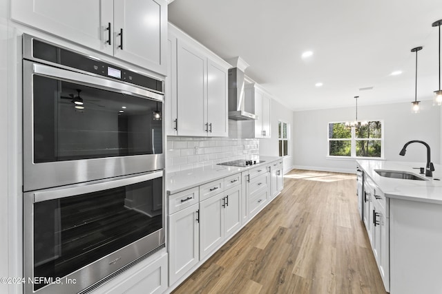 kitchen featuring light stone countertops, stainless steel double oven, sink, white cabinetry, and hanging light fixtures