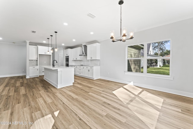 kitchen featuring a kitchen island with sink, wall chimney exhaust hood, light wood-type flooring, decorative light fixtures, and white cabinetry