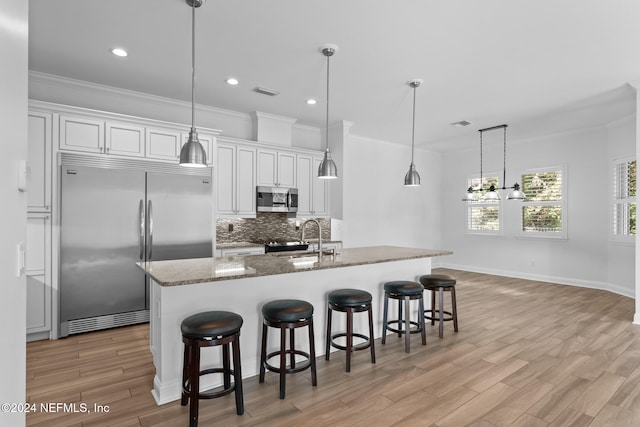 kitchen with stone counters, white cabinetry, hanging light fixtures, appliances with stainless steel finishes, and light wood-type flooring