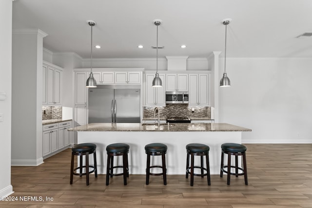 kitchen featuring hardwood / wood-style floors, a kitchen island with sink, hanging light fixtures, appliances with stainless steel finishes, and a kitchen bar