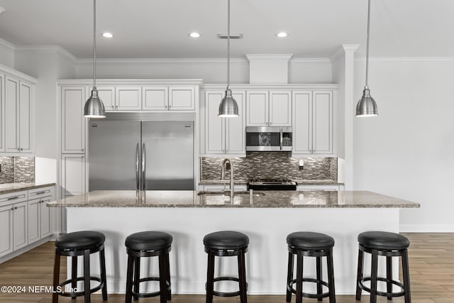 kitchen with sink, stainless steel appliances, hardwood / wood-style floors, pendant lighting, and a center island with sink