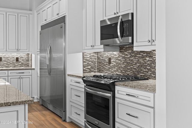 kitchen featuring decorative backsplash, appliances with stainless steel finishes, light hardwood / wood-style floors, light stone counters, and white cabinetry