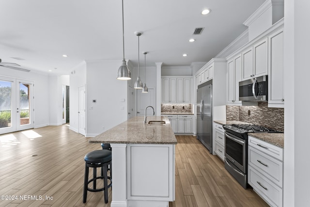 kitchen with ornamental molding, stainless steel appliances, sink, a center island with sink, and light hardwood / wood-style flooring