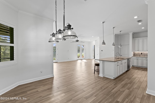 kitchen featuring a center island with sink, sink, decorative light fixtures, light hardwood / wood-style floors, and a kitchen bar