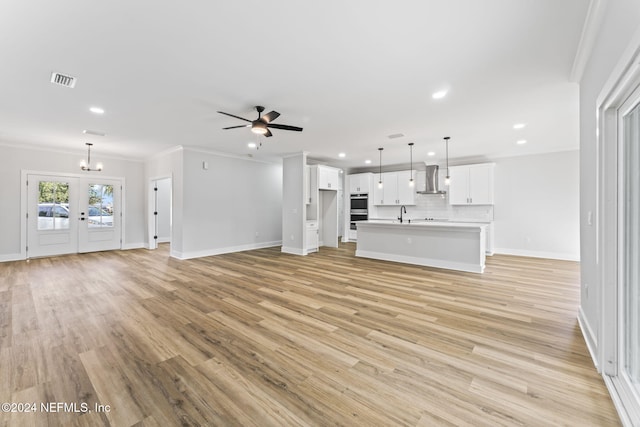 unfurnished living room featuring ornamental molding, ceiling fan with notable chandelier, and light hardwood / wood-style floors