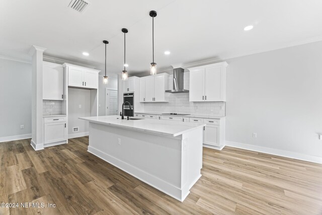 kitchen featuring wall chimney exhaust hood, an island with sink, and white cabinets