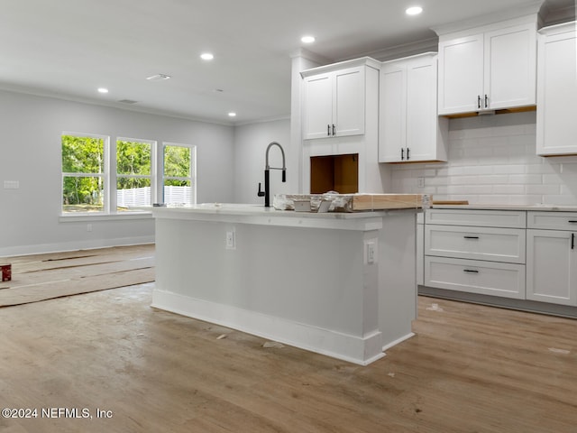 kitchen featuring light wood-type flooring, a center island with sink, white cabinetry, and backsplash