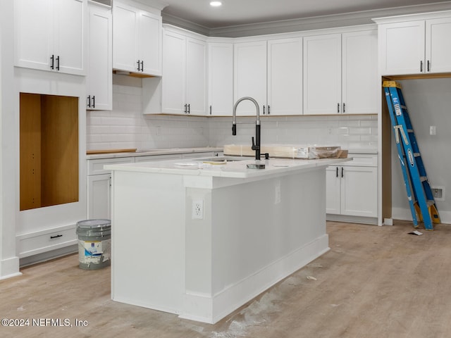 kitchen with white cabinets, light hardwood / wood-style floors, and a kitchen island with sink