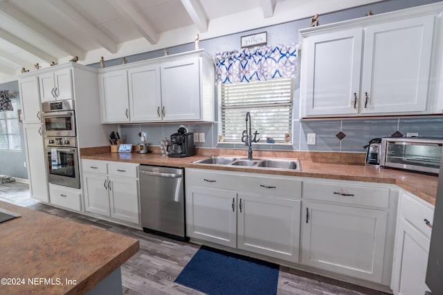 kitchen featuring white cabinets, beam ceiling, sink, and stainless steel appliances