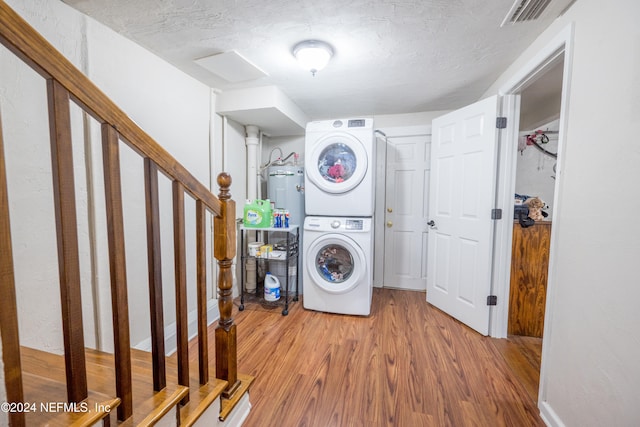 laundry area with hardwood / wood-style floors, a textured ceiling, stacked washer / dryer, and water heater