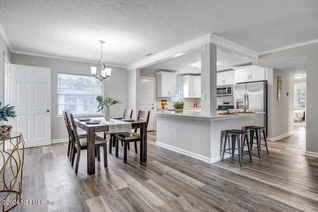 dining room with hardwood / wood-style floors, a chandelier, a textured ceiling, and ornamental molding