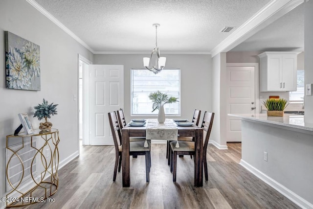 dining space with light hardwood / wood-style floors, ornamental molding, a textured ceiling, and an inviting chandelier