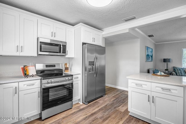 kitchen with ornamental molding, a textured ceiling, stainless steel appliances, hardwood / wood-style flooring, and white cabinetry