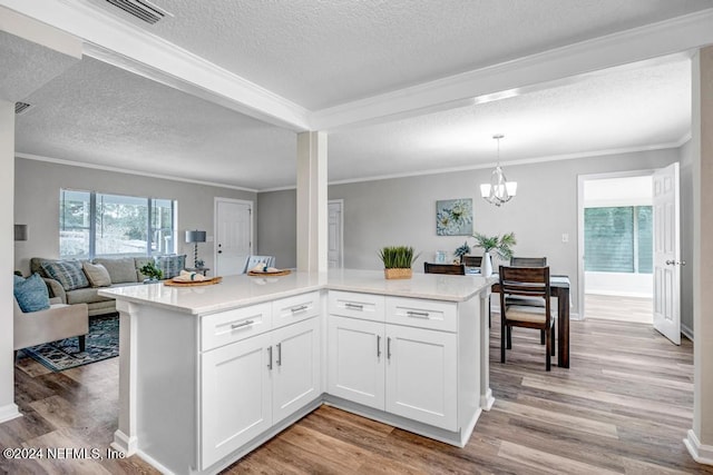 kitchen featuring pendant lighting, light hardwood / wood-style floors, a textured ceiling, white cabinets, and ornamental molding