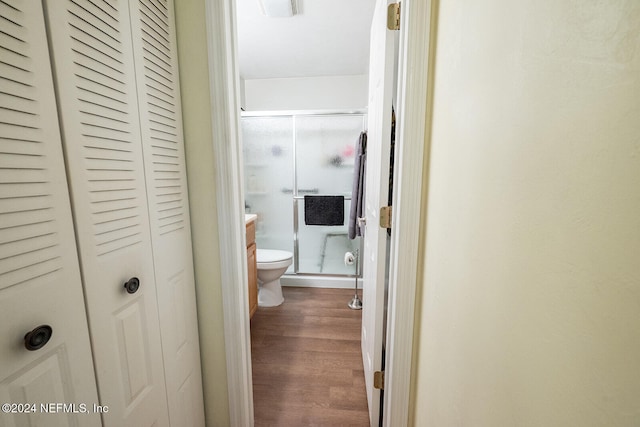 bathroom with wood-type flooring, vanity, toilet, and a shower with shower door