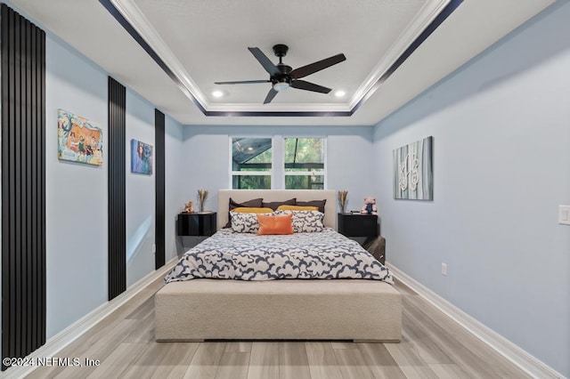 bedroom with ceiling fan, a raised ceiling, light wood-type flooring, and ornamental molding